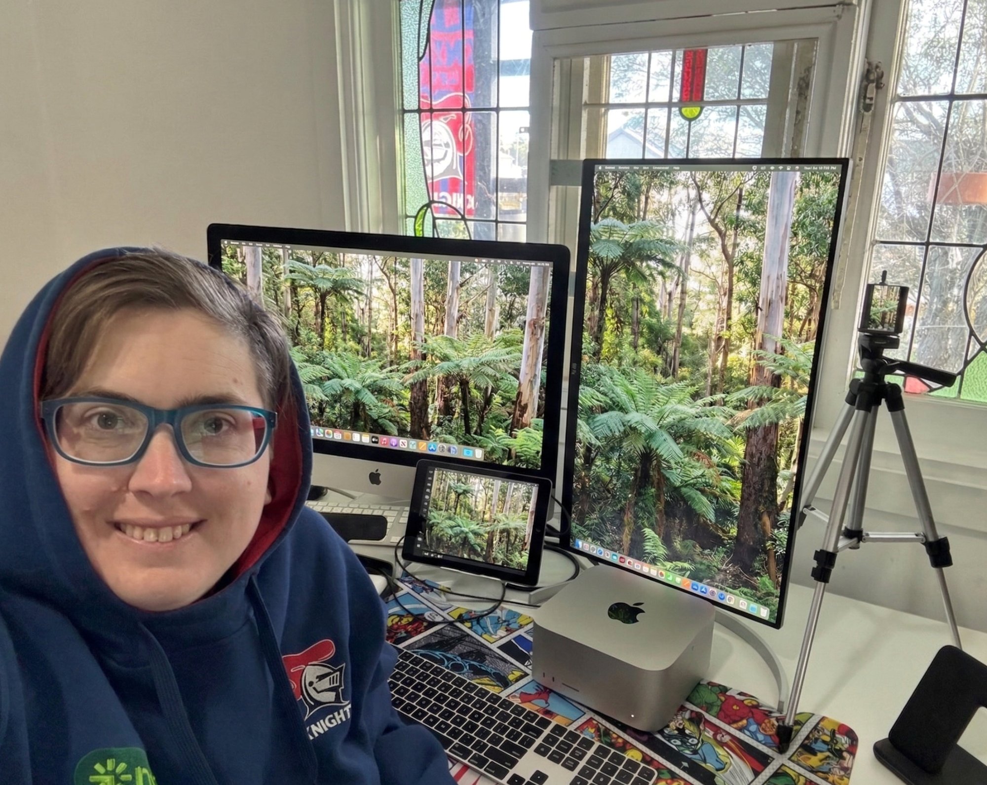 Jess at her desk with Mac Studio, dual monitors, and a comic book desk mat