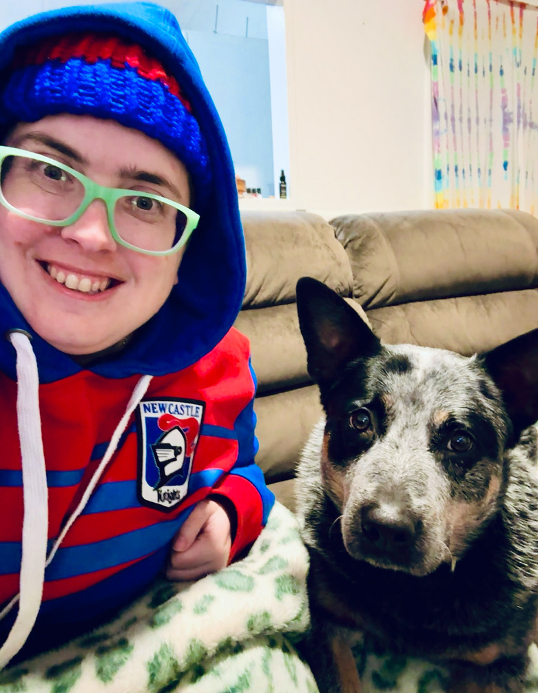 Jess in a Newcastle Knights hoodie with Ash the cattle dog on the couch