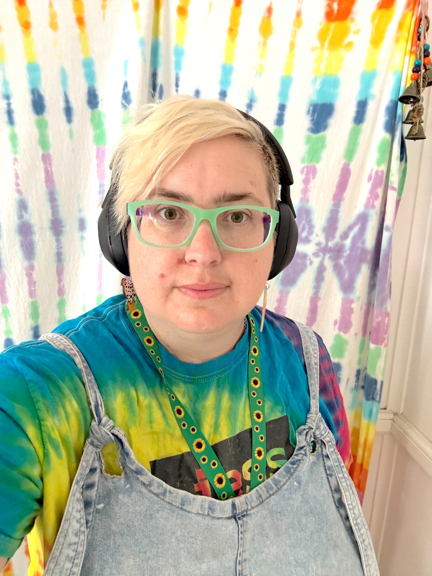 Jess Jones wearing green glasses and a tie-dye shirt, smiling at the camera