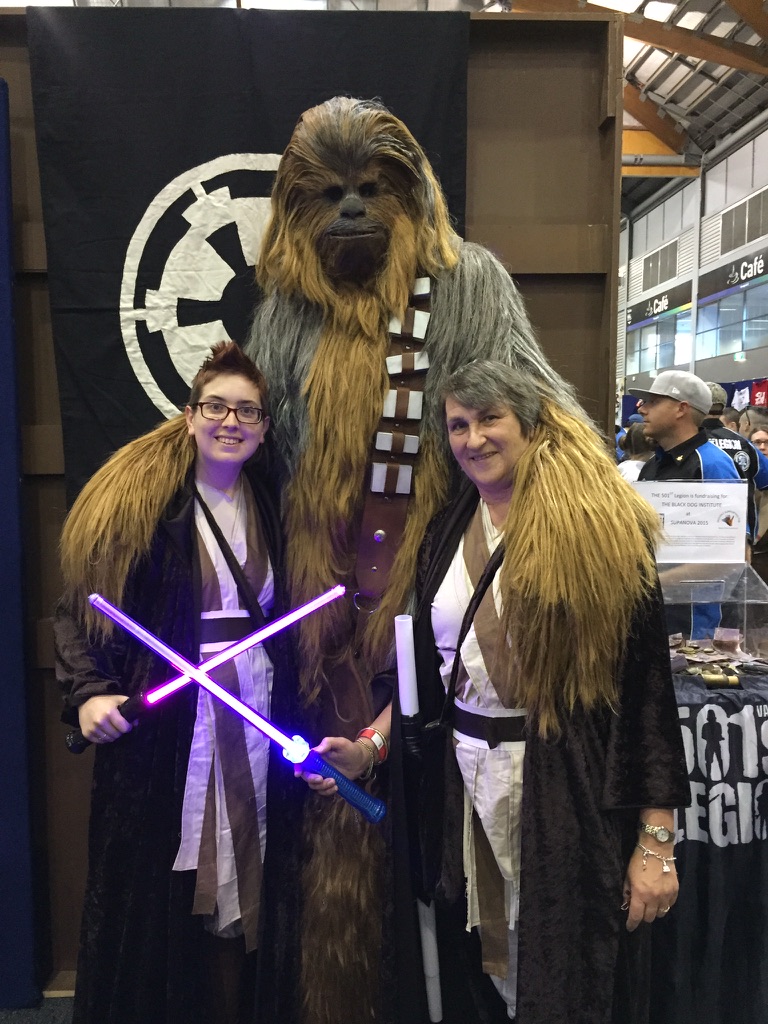 Jess and her mum in Jedi cosplay with a Chewbacca at Supanova, lightsabers crossed