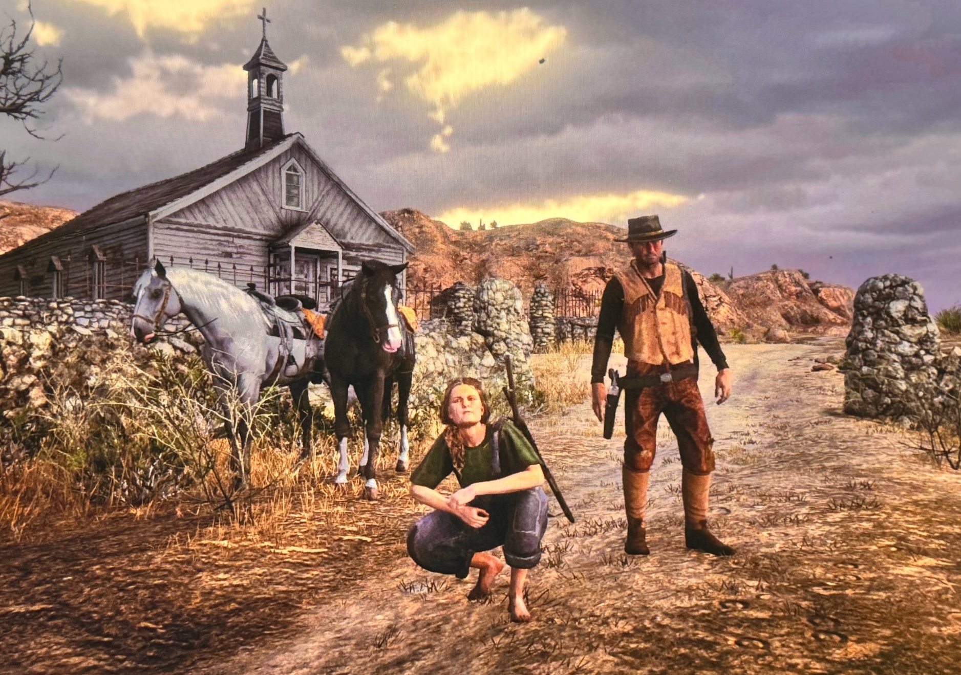 Red Dead Redemption 2 screenshot with two characters and horses outside a church at sunset
